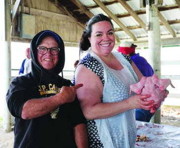 Two people stand under an open barn. One holds up a raw chicken